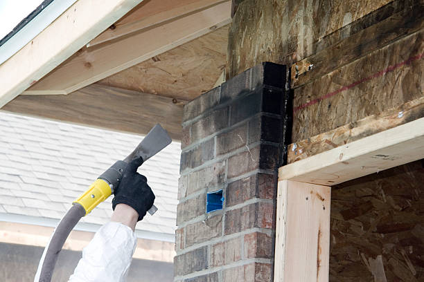 The image shows a person using a power tool or sander to work on exposed wooden beams and brick chimney during what appears to be a home renovation or construction project.